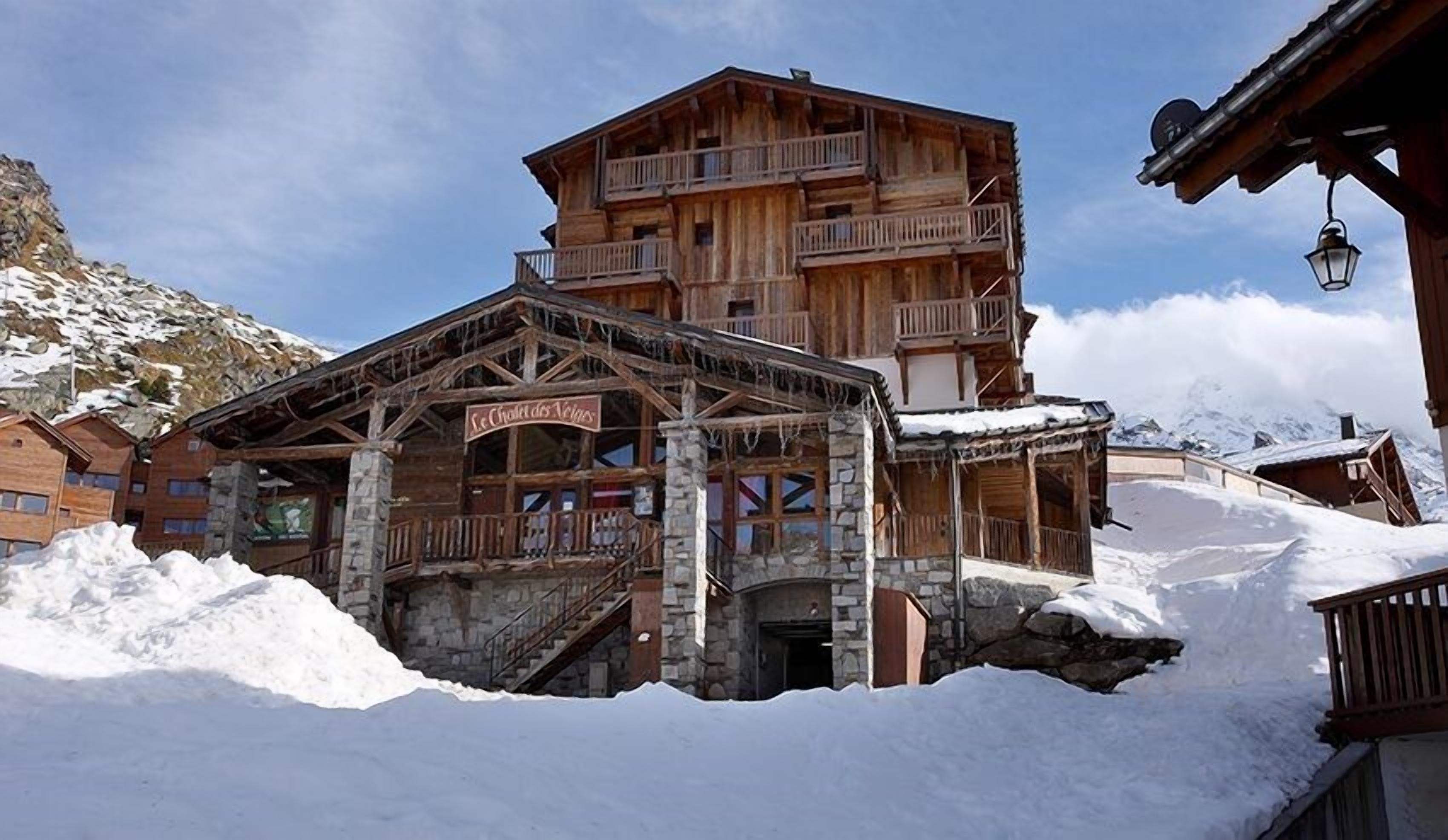 A wooden chalet with a stone staircase and balconies, surrounded by snow.