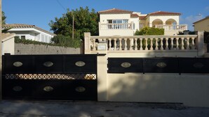 Una proprietà residenziale recintata con facciata bianca, tetto in tegole e un balcone con colonne.