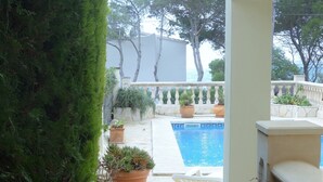 Area piscina con parete bianca, piante in vaso e vista libera sul mare.