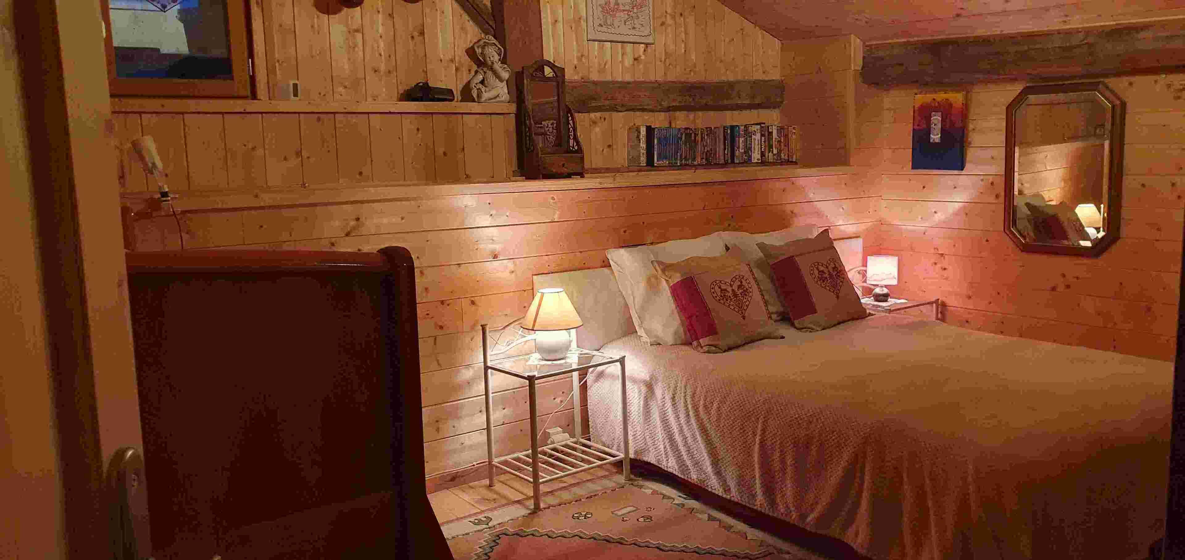Ein gemütlicher Holzraum mit einem Bett, einem Nachttisch, einer Lampe und einem Spiegel.
