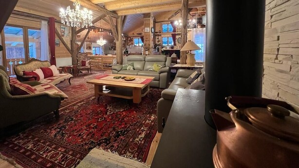 Un interior acogedor y rústico con vigas de madera, una araña, una chimenea y un ventanal grande.