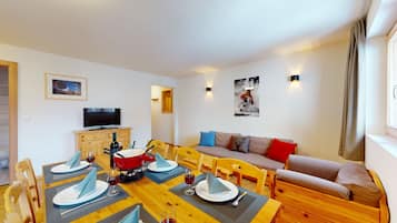 Comedor con mesa de madera dispuesta para cuatro personas, un sofá y un televisor sobre un mueble de madera.