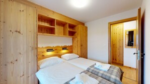 A wooden room with a bed, a small shelf, and a door.