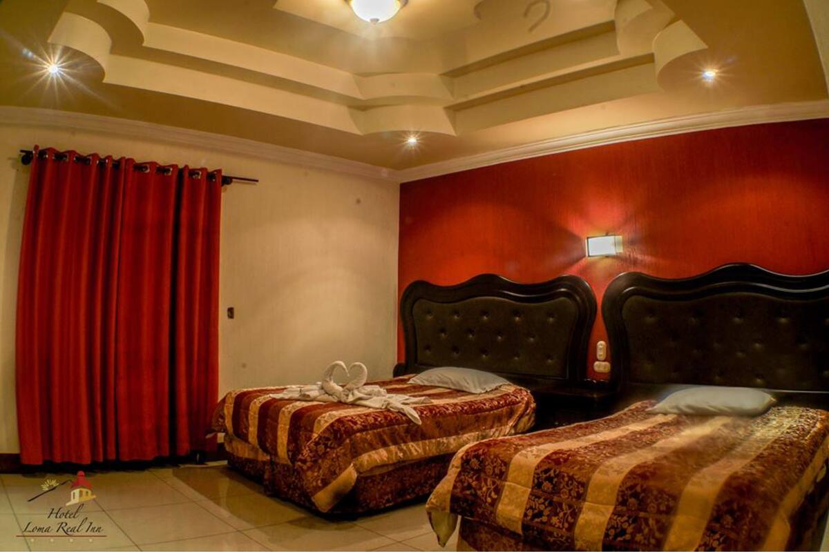 A hotel room with two beds, red curtains, a red wall, and a ceiling with recessed lighting.