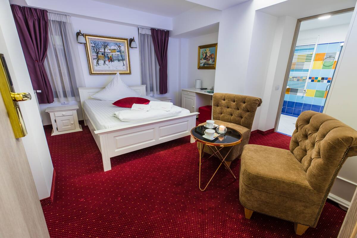 A hotel room with a bed, a chair, a small table, and a desk.