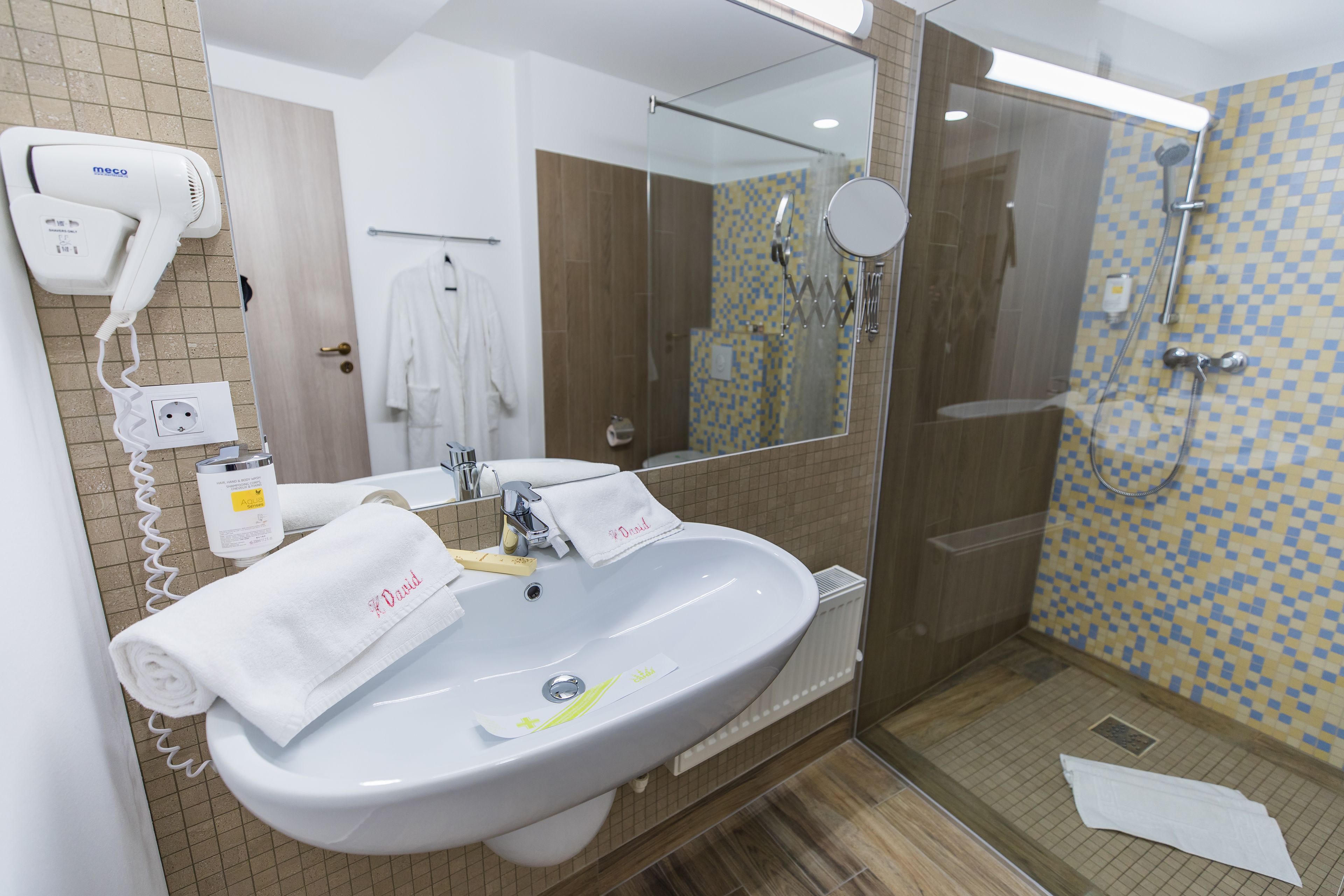 A bathroom with a white sink, a hairdryer, a mirror, and a shower area.