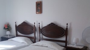 A bedroom with two wooden beds, a bedside table with a lamp, and a wall-mounted picture. - Hostel Pereira is on the first floor of a detached villa (Loulé)