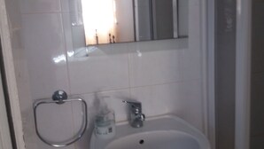 A bathroom with a white sink, a mirror, and a shower area. - Hostel Pereira is on the first floor of a detached villa (Loulé)