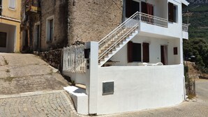 A two-story building with a white exterior, a stone wall, and a staircase leading to the upper floor.