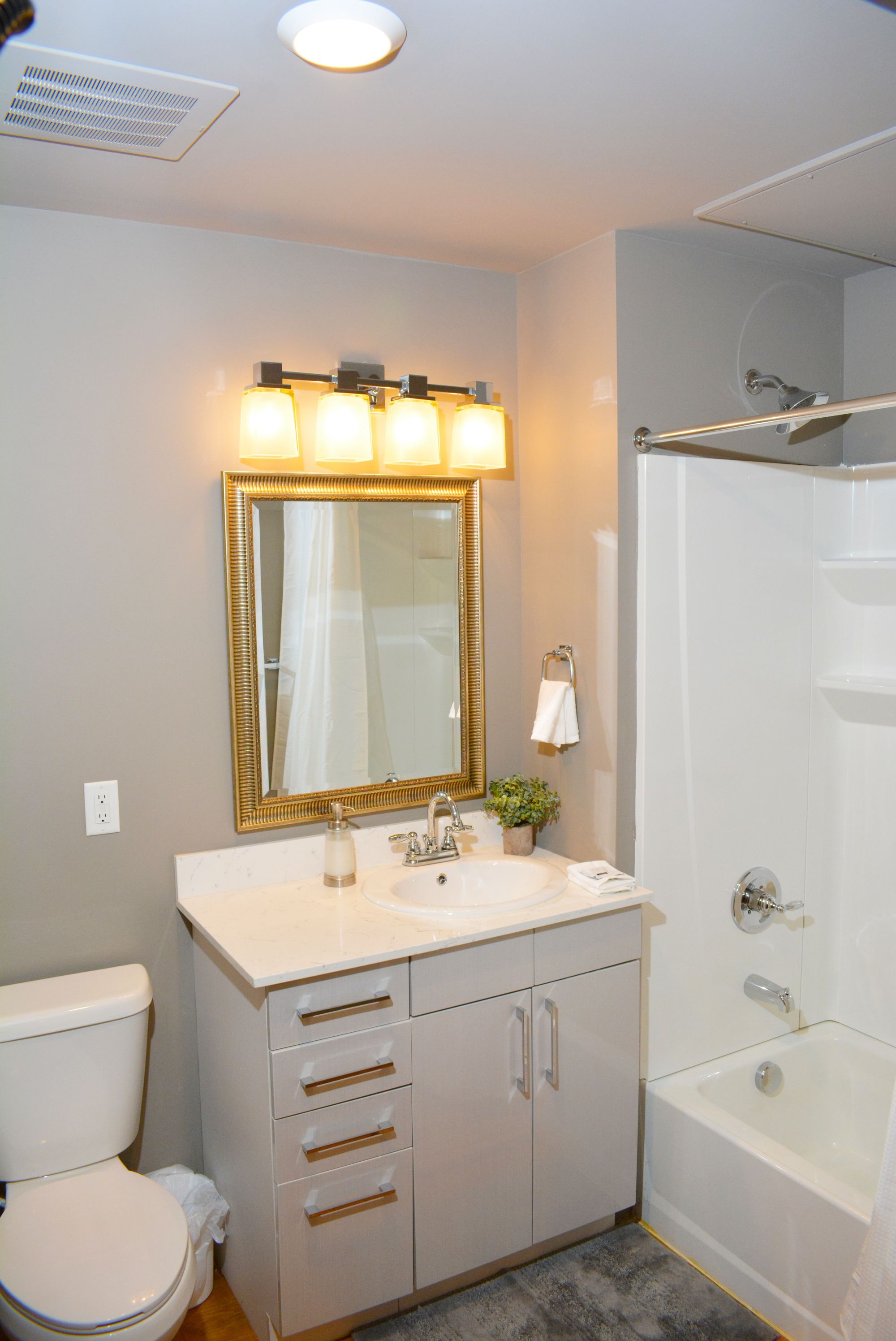 A bathroom with a toilet, sink, vanity with drawers, a mirror, and a bathtub.