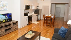 Uma cozinha moderna com armários brancos, eletrodomésticos de aço inoxidável e um espaço de refeições com cadeiras e mesa de madeira.