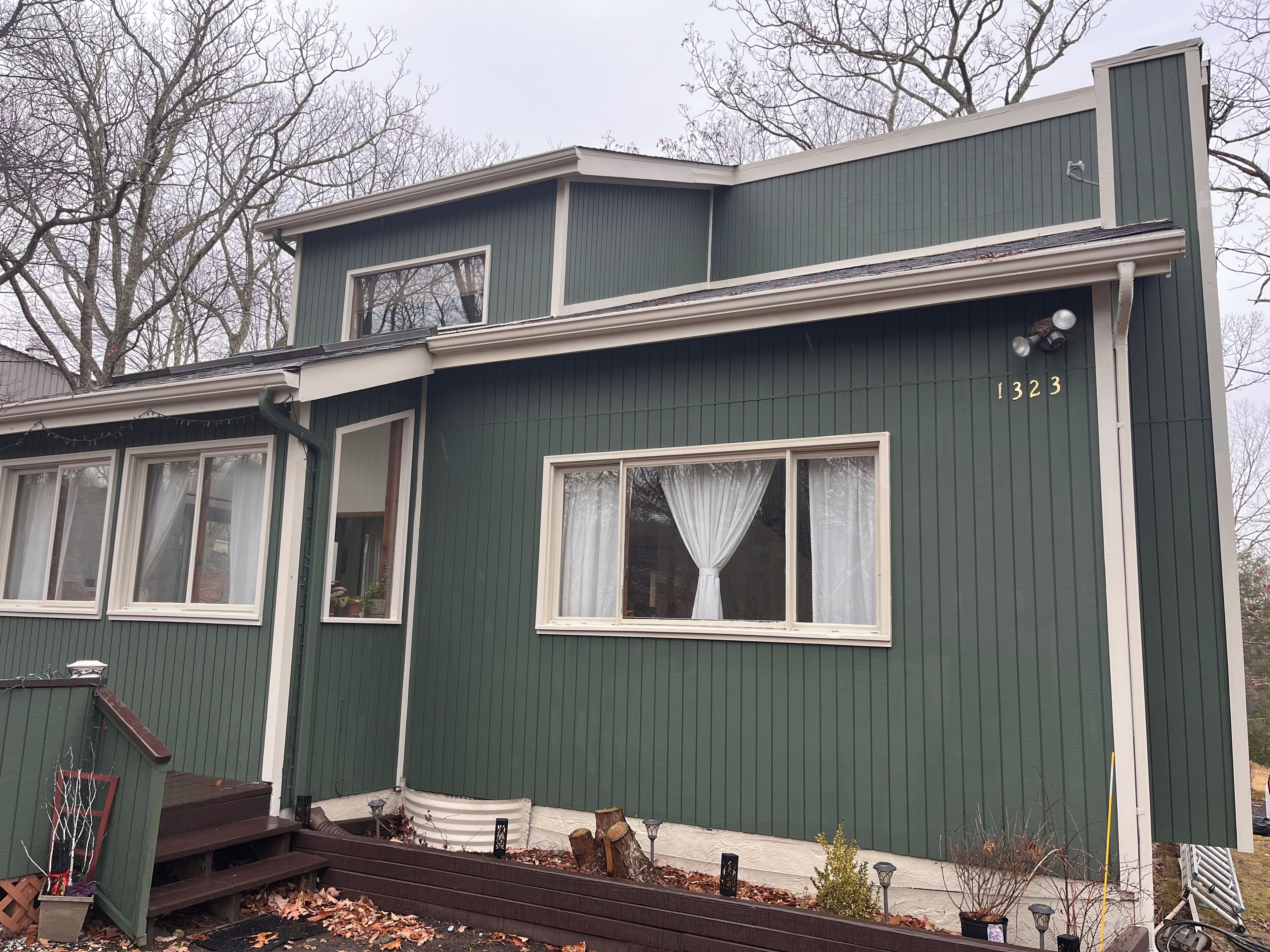 A green building with a number 1323 on the side, a front porch with steps, and a window with a curtain.