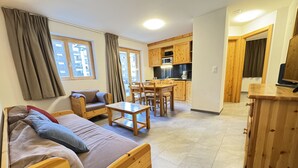 A cozy room with a wooden bed, a sofa, a dining table, and a kitchen area with wooden cabinets and a microwave. - Pracondu 2 001 - OUTDOOR & FUN  charming apartment (Haute-Nendaz)