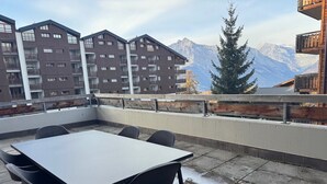 A rooftop terrace with a table and chairs, overlooking a mountain range and residential buildings. - Pracondu 2 001 - OUTDOOR & FUN  charming apartment (Haute-Nendaz)