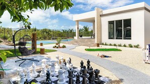 A modern outdoor area with a chessboard, a swing chair, and a pool. - SPECIAL DISC, 3BR PRIVATE VILLA, OCEAN VIEW, GREAT AMENITIES, STEPS TO THE BEACH (Long Bay Hills)