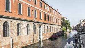 A canal with boats, a brick building with arched windows, and a row of other buildings along the water. - Elegant Fornasa Vecia Canal View R&R (Venecia)