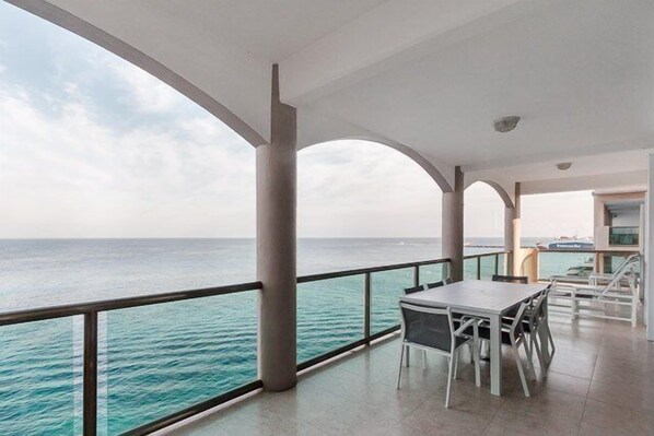 A balcony with a view of the sea, a table and chairs, and a railing. - In The Heart of Cozumel (Cozumel)