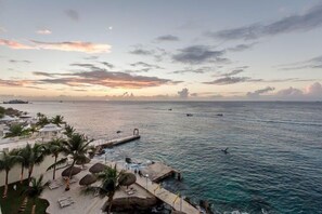 A coastal resort with a pool area, palm trees, and a pier extending into the sea. - In The Heart of Cozumel (Cozumel)
