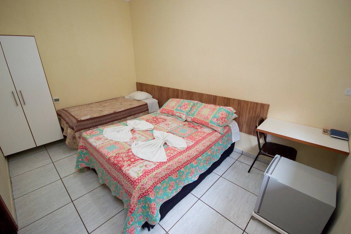 A bedroom with a bed, a desk, a wardrobe, and a refrigerator.