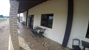 Un espacio al aire libre con techo, mesas y sillas, suelo de baldosas y un pilar de ladrillo.