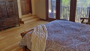 Une chambre avec un grand lit, une commode en bois, un tapis à motifs et un balcon offrant une vue sur des formations rocheuses rouges.