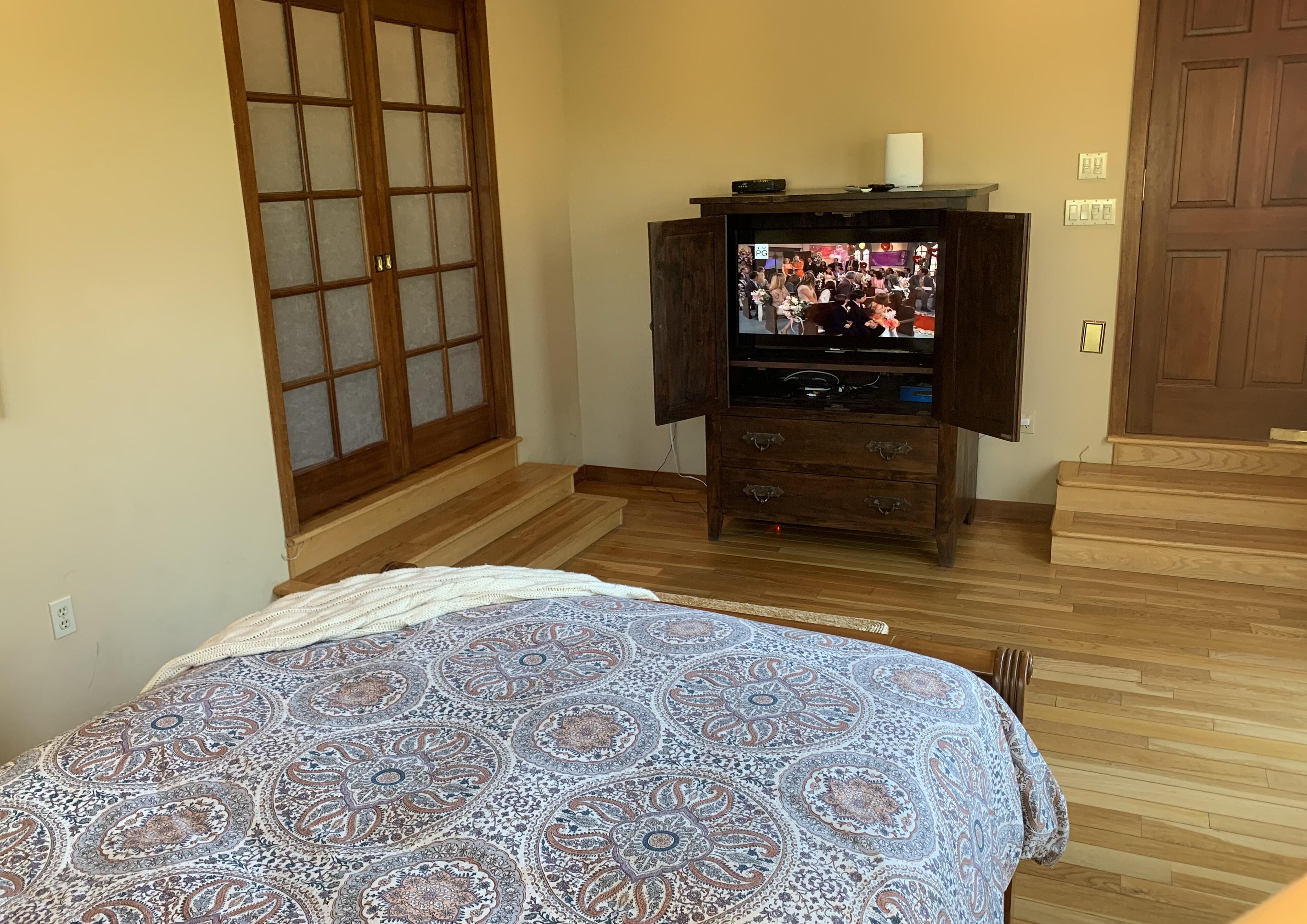 A bedroom with a bed, a wooden dresser, a television, and a sliding door.