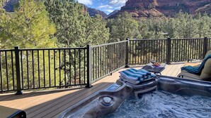 Un bain à remous sur une terrasse en bois, avec vue sur les montagnes, entouré d’une rambarde noire.