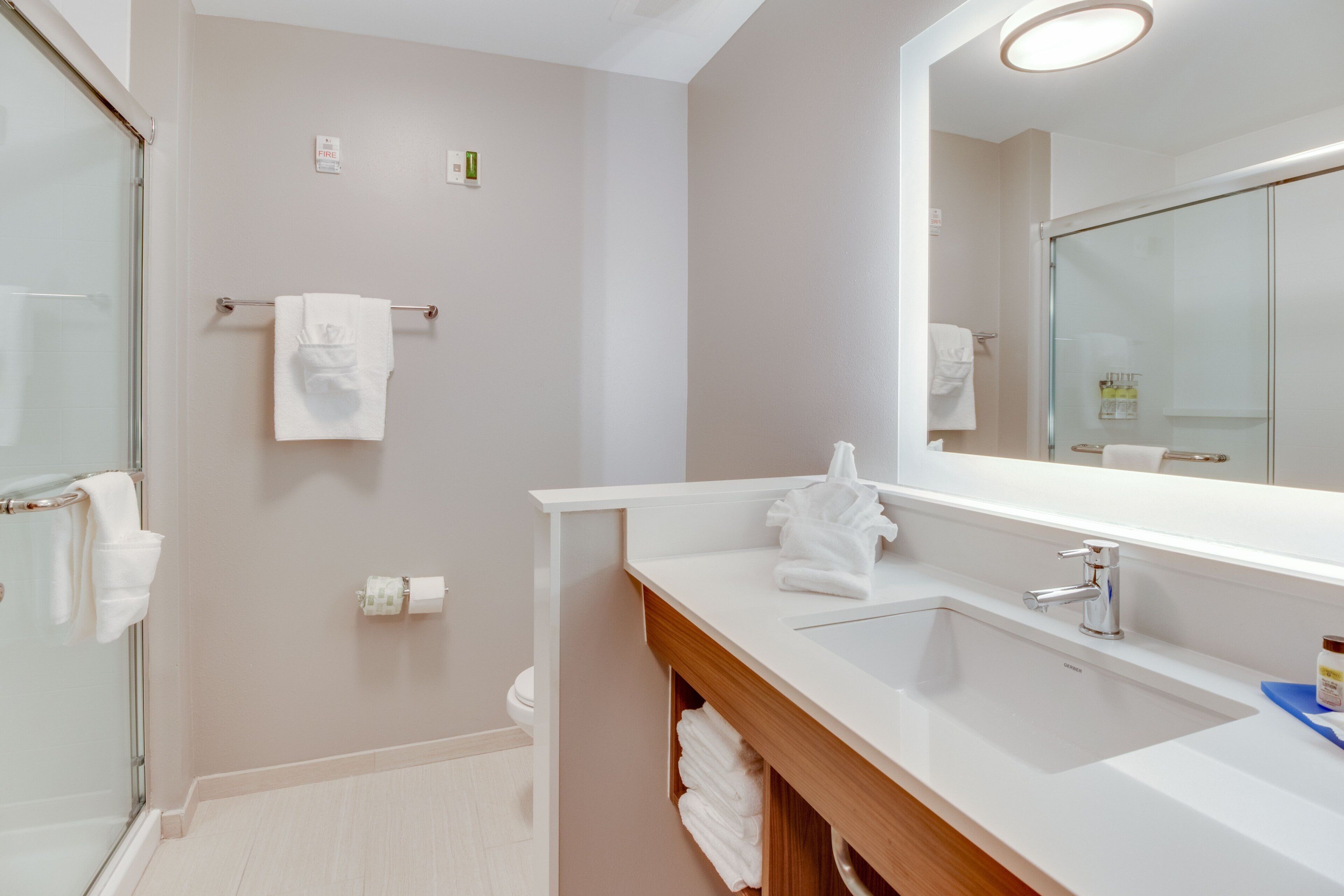 Une salle de bain moderne avec une douche à parois de verre, un grand miroir et un meuble-lavabo doté d’un évier et d’un porte-serviettes.