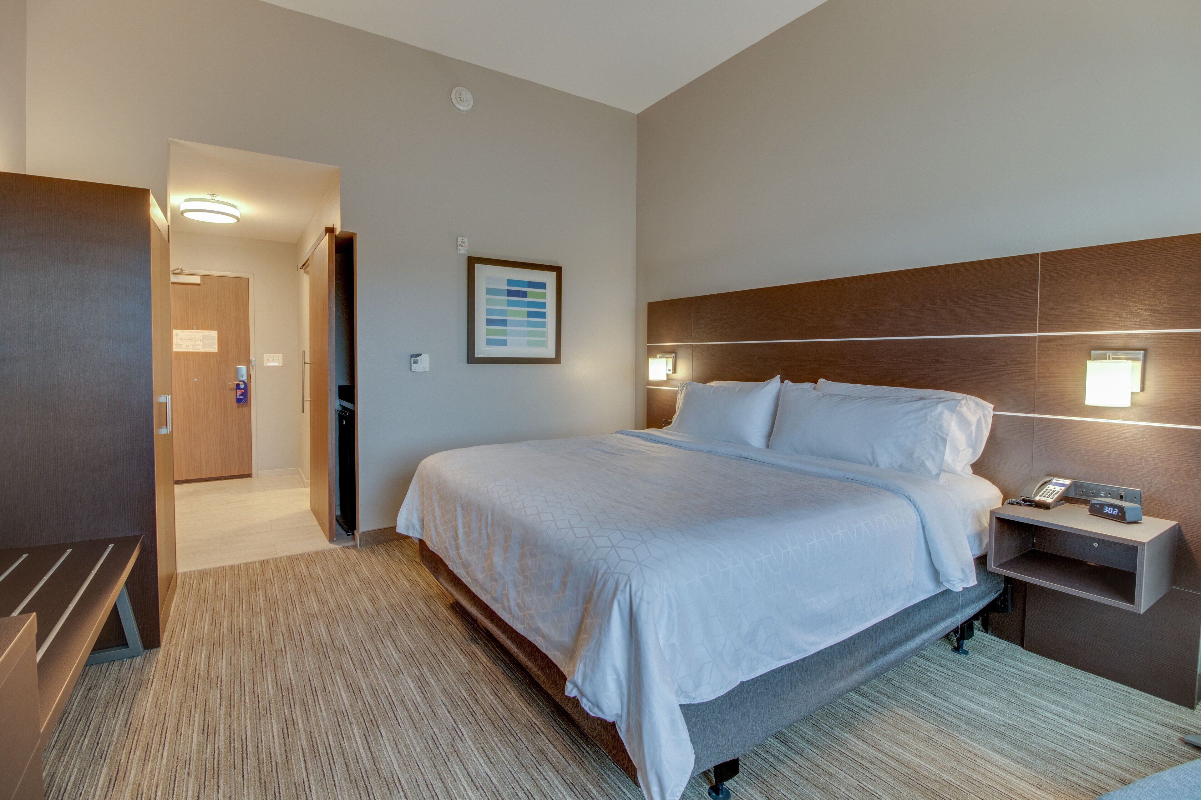 A hotel room with a large bed, bedside tables, a desk, and a bathroom visible through an open door.