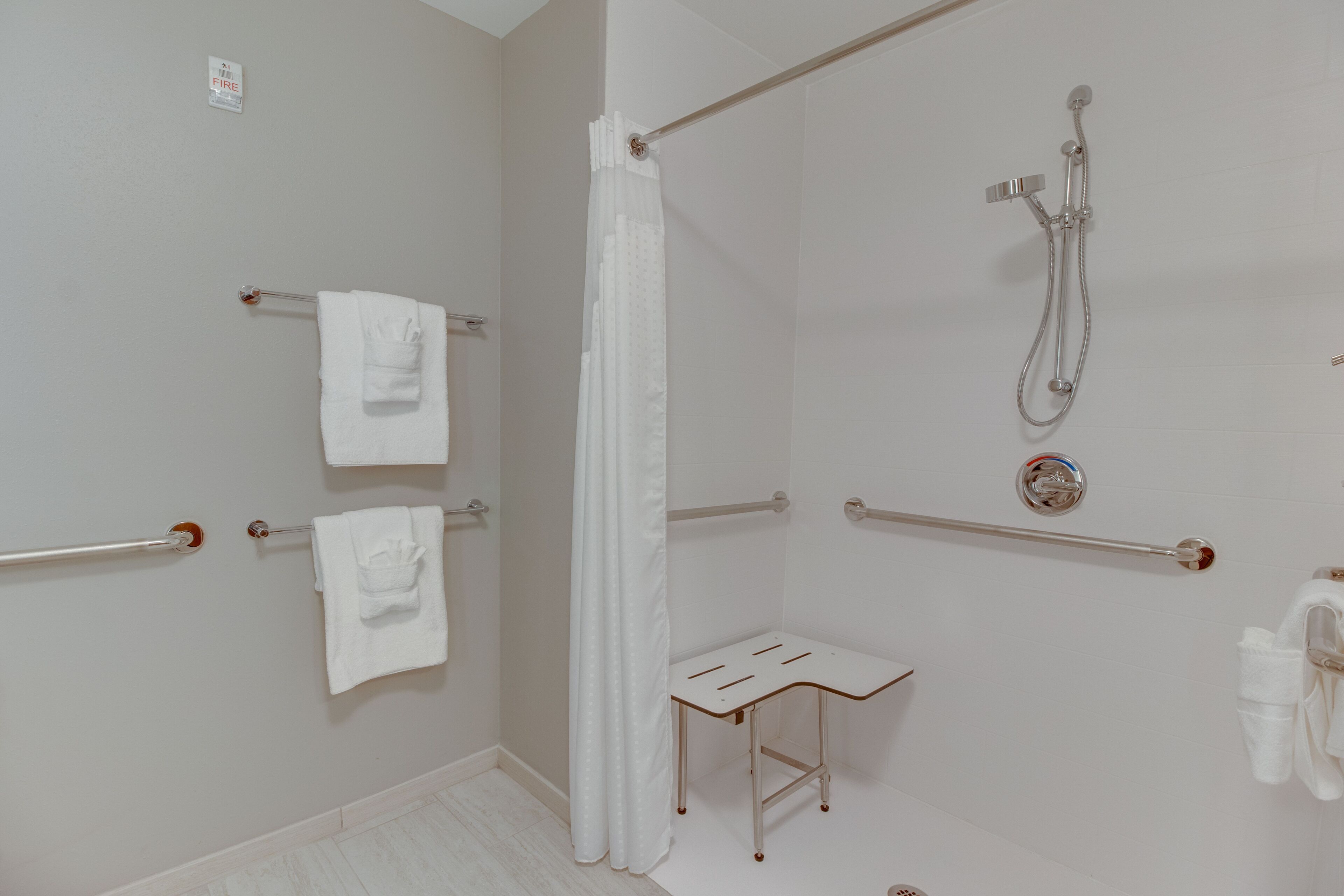 A bathroom with a shower, grab bars, a towel rack, and a small table.