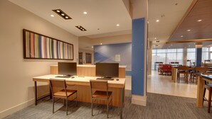 A modern office space with a long desk, two chairs, and a computer. There are multiple tables and chairs in the background, and a colorful striped artwork on the wall. - Holiday Inn Express & Suites Union City by IHG (Union City)