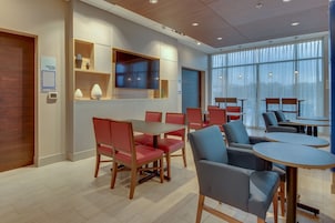 Una sala de reuniones moderna con sillas rojas y grises, un televisor de pantalla plana grande y un mueble de madera con adornos.