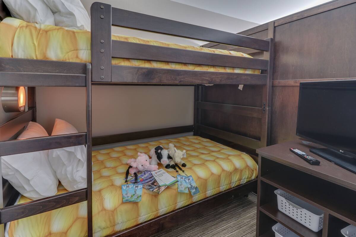 A bunk bed with a mattress, pillows, stuffed toys, and a remote control on a wooden shelf.