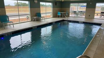 Une piscine intérieure à l’eau claire, dotée d’indications de profondeur pour assurer la sécurité et d’espaces aménagés avec des chaises et des tables.