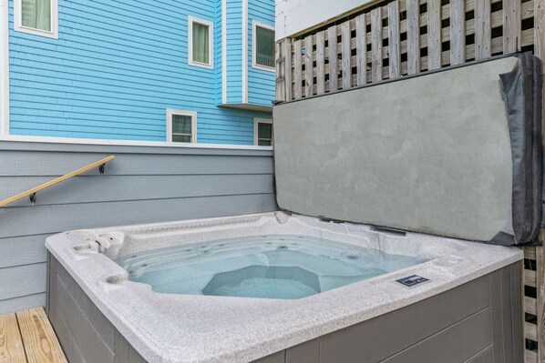 A hot tub with a stone exterior, a wooden deck, and a blue building in the background. - Premier Oceanfront Home with Pool, Hot Tub, Elevator, Sauna, Game Room, Theater (Hatteras)