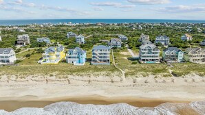 A coastal residential area with beachfront properties featuring multi-story houses with balconies, some with visible staircases leading to upper floors. - Premier Oceanfront Home with Pool, Hot Tub, Elevator, Sauna, Game Room, Theater (Hatteras)