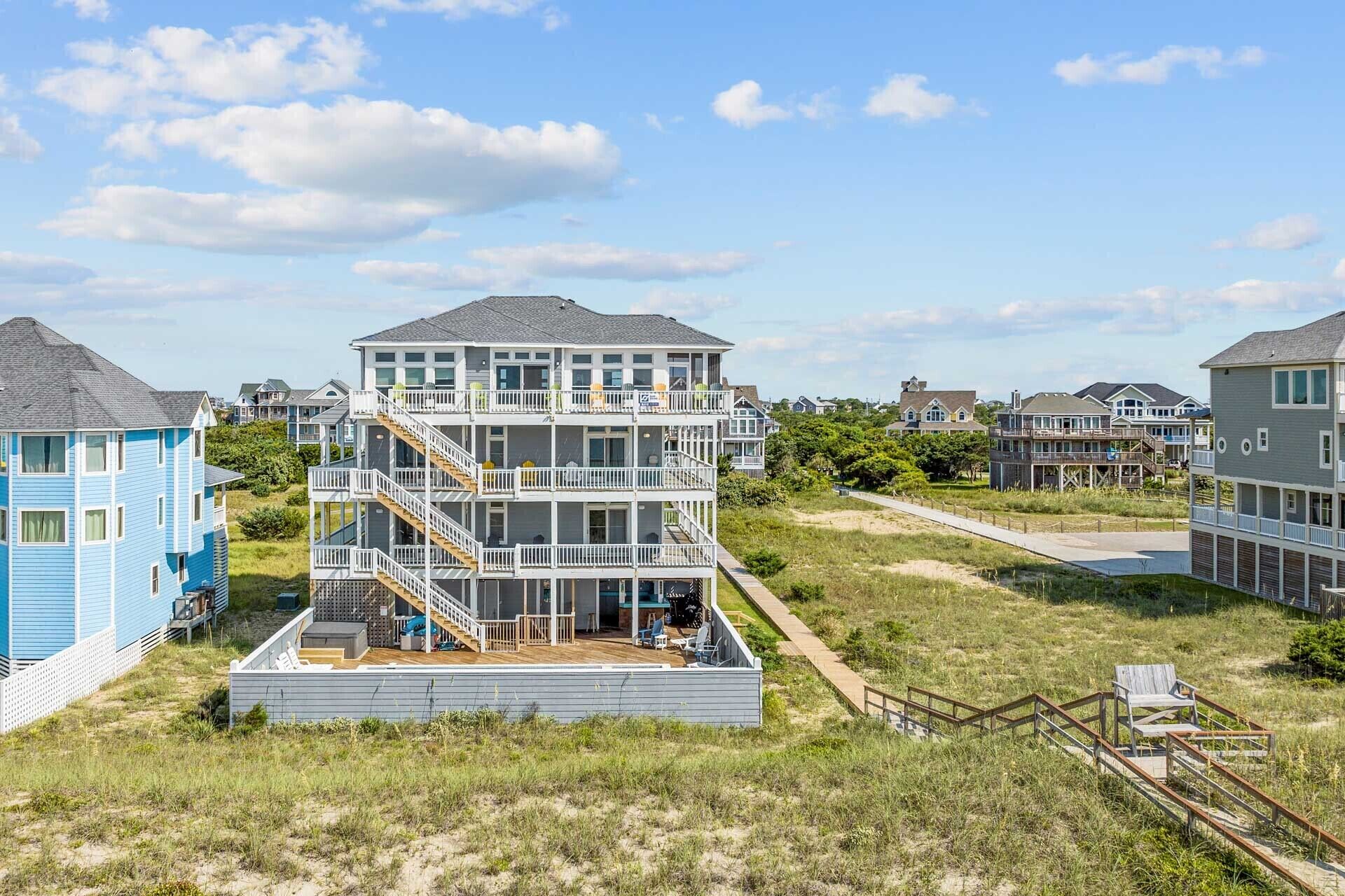 A multi-story beachfront property with a prominent staircase, a deck, and a sandy beach area.