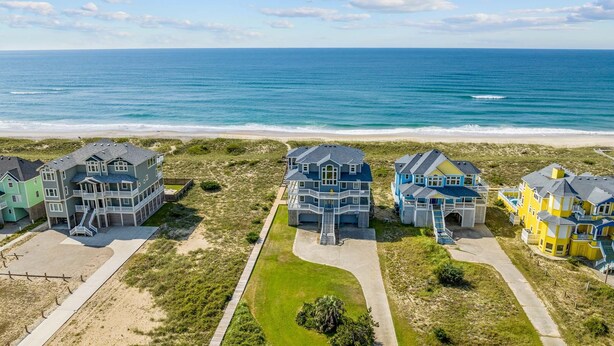 A beachfront property with multiple houses, a sandy beach, and the ocean in the background. - Premier Oceanfront Home with Pool, Hot Tub, Elevator, Sauna, Game Room, Theater (Hatteras)