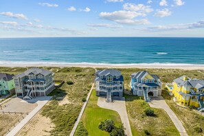 A beachfront property with multiple houses, a sandy beach, and the ocean in the background. - Premier Oceanfront Home with Pool, Hot Tub, Elevator, Sauna, Game Room, Theater (Hatteras)
