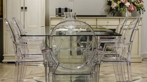 Una cocina moderna con una mesa de comedor de vidrio, sillas traslúcidas y suelo de baldosas.