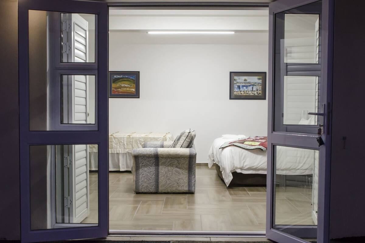 A room with a bed, a chair, and a small table. There are two framed pictures on the wall.