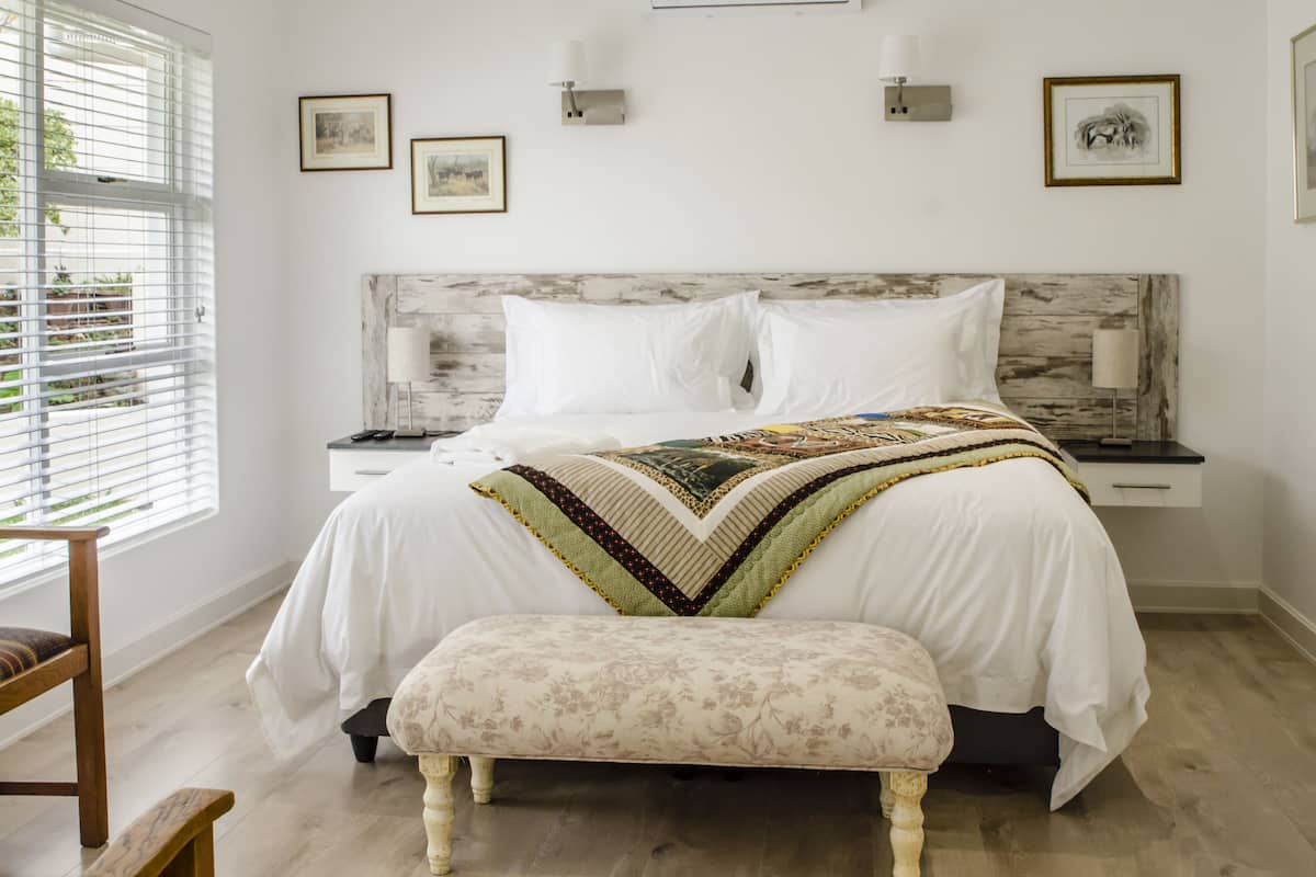 A bedroom with a large bed, a bench, bedside tables, wall-mounted lamps, and framed pictures on the wall.