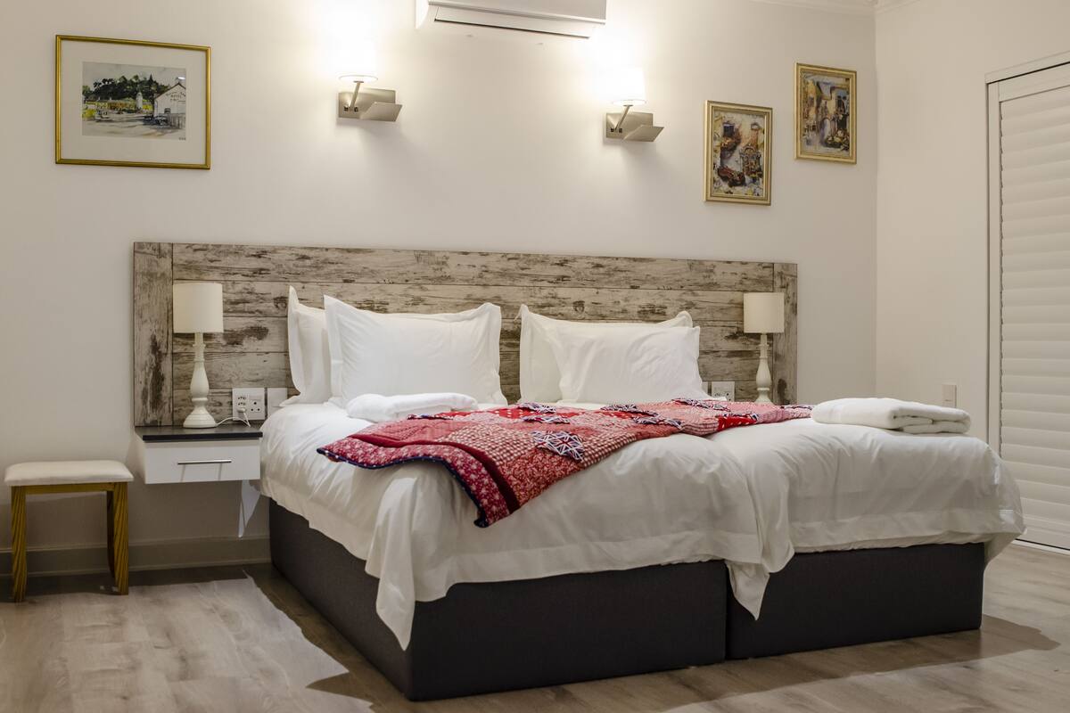 A neatly made bed with white linens and a red blanket, a bedside table with a lamp, and wall-mounted light fixtures.