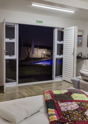 A room with a sliding glass door leading to an outdoor area, a patterned quilt on the bed, and a small kitchenette area. - Somerset View Guest House (Cape Town)