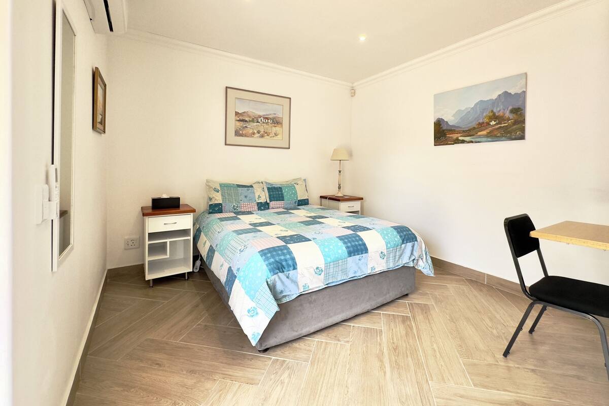 A bedroom with a bed, bedside table, chair, and two paintings on the wall.