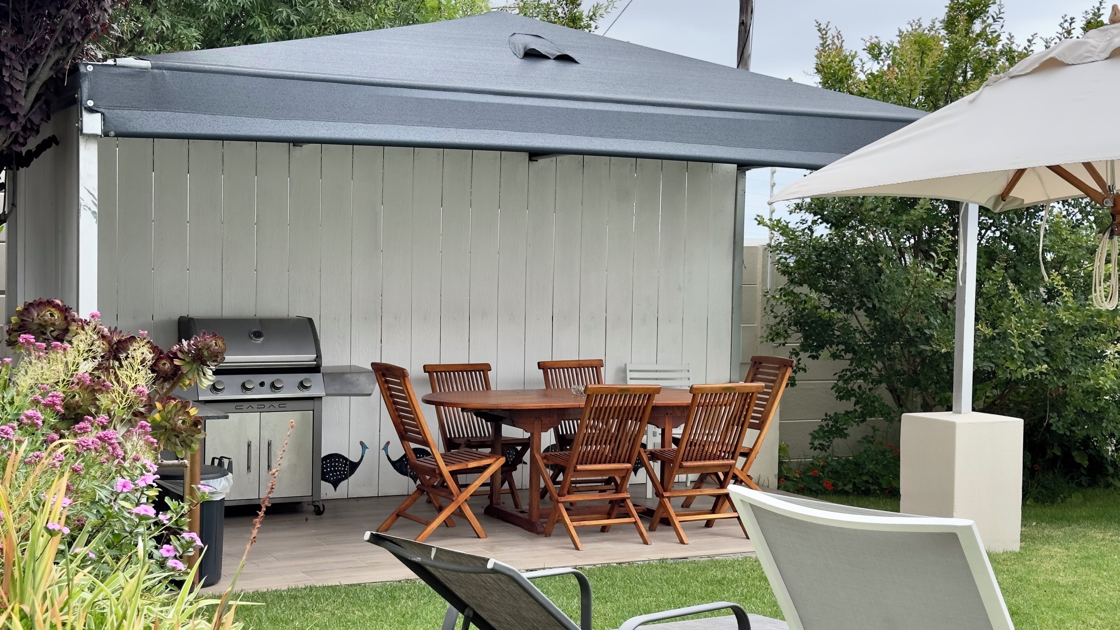 Une terrasse avec un barbecue, une table en bois et des chaises.