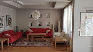 A modern living room with a red sofa, a beige sofa, and a coffee table. There are framed artworks on the walls and a large abstract painting on the right. - Luxury Villa, Scandinavian style,in Golf Solimanya (Giza)