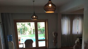 A spacious room with a tiled floor, a large sliding glass door leading to a pool, and a hanging light fixture. - Luxury Villa, Scandinavian style,in Golf Solimanya (Giza)