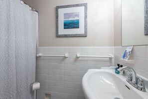 Un baño con un lavamanos blanco, un cuadro en la pared y un perchero para toallas.