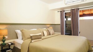 Habitación de hotel con una cama, una mesita de noche, una lámpara, una ventana con cortinas y un equipo de aire acondicionado.
